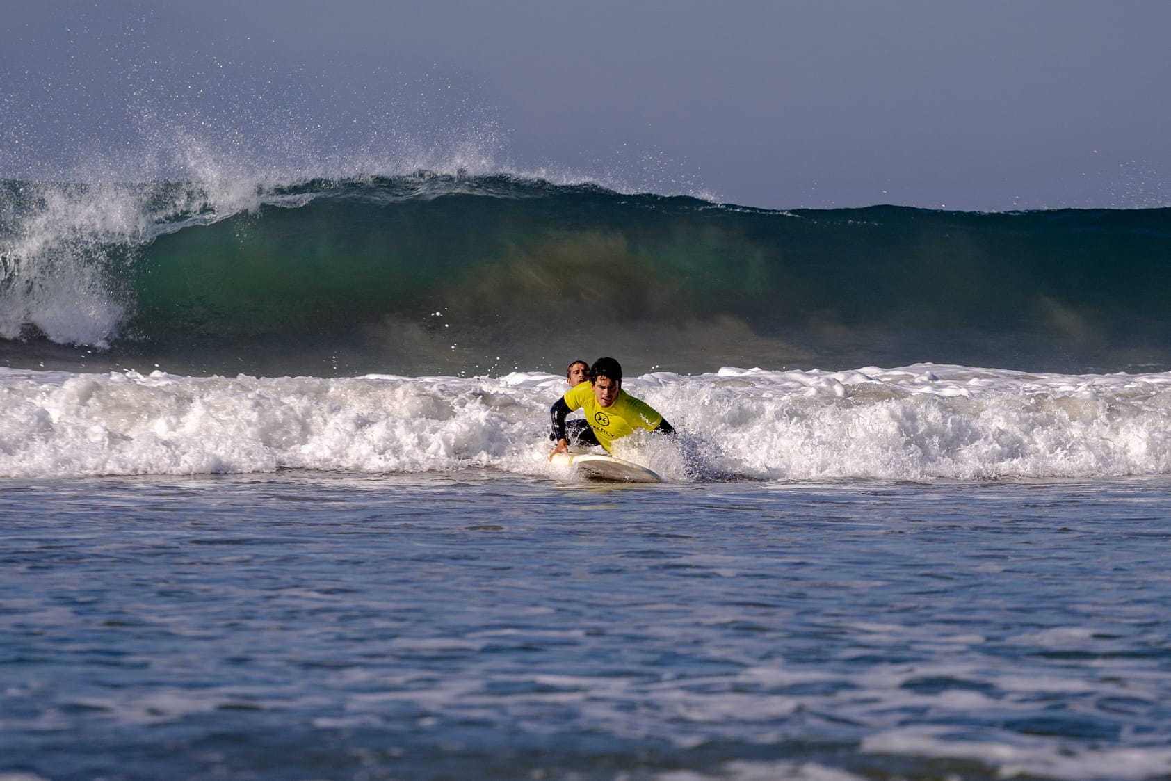 Surf instructor guiding a student through a wave on Portugal's Atlantic coast